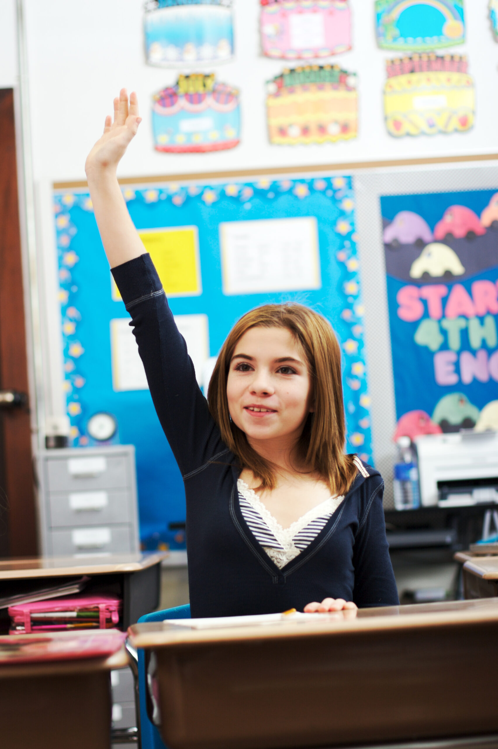 Young girl in classroom raises her hand