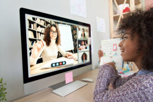 Cute african kid child girl showing homework talking to remote teacher distance learning during virtual online class on video conference call with tutor and school children group at home on computer.